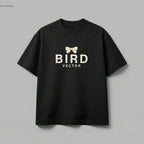 Cream ribbon bow graphic on a black t-shirt. 180gsm organic ringspun cotton featuring BIRD VECTOR minimalist text branding.